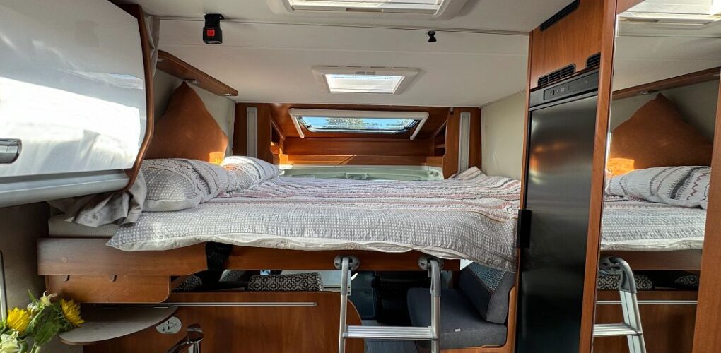 Het drop down tweepersoonsbed voorin de Britz Odyssey camper inclusief ladder en dakraam