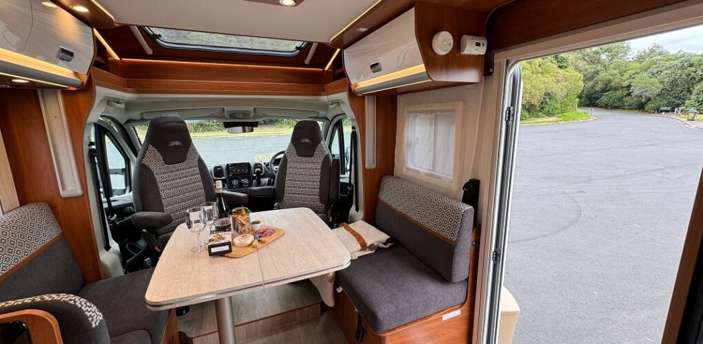 Het zitgedeelte van de Britz Odyssey camper in Nieuw-Zeeland met twee draaibare stoelen in de bestuurdersruimte, borrelplank op tafel en twee bankjes