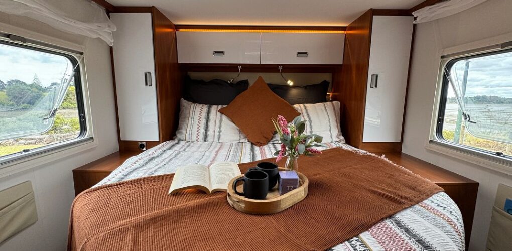 Het tweepersoonsbed achterin de Britz Odyssey camper met kastruimte en loopruimte aan beide kanten van het bed inclusief ramen met uitzicht op de natuur van Nieuw-Zeeland