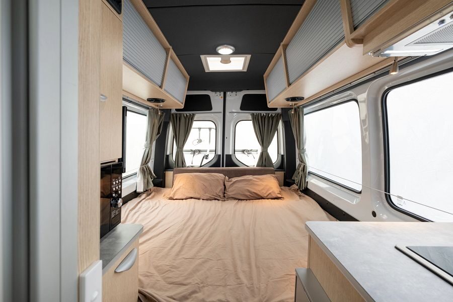 Een opgemaakt tweepersoonsbed achterin de Maui Ultima Plus camper met daarboven opbergruimte