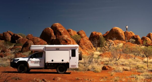 De camperreiziger is uit de RedSands camper gestapt om bovenop een rotsblok van het uitzicht te genieten