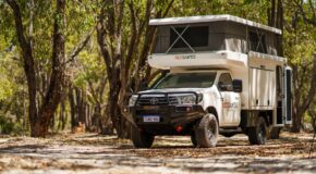 De RedSands camper met uitgeklapt dak staat in een schaduwrijke plek tussen de bomen