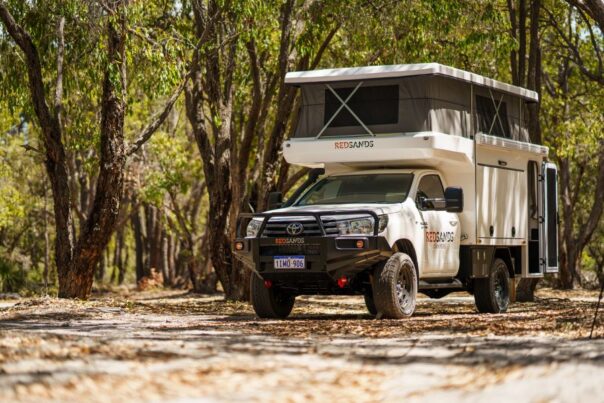 De RedSands camper met uitgeklapt dak staat in een schaduwrijke plek tussen de bomen