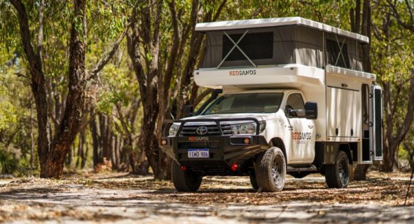 De RedSands camper met uitgeklapt dak staat in een schaduwrijke plek tussen de bomen