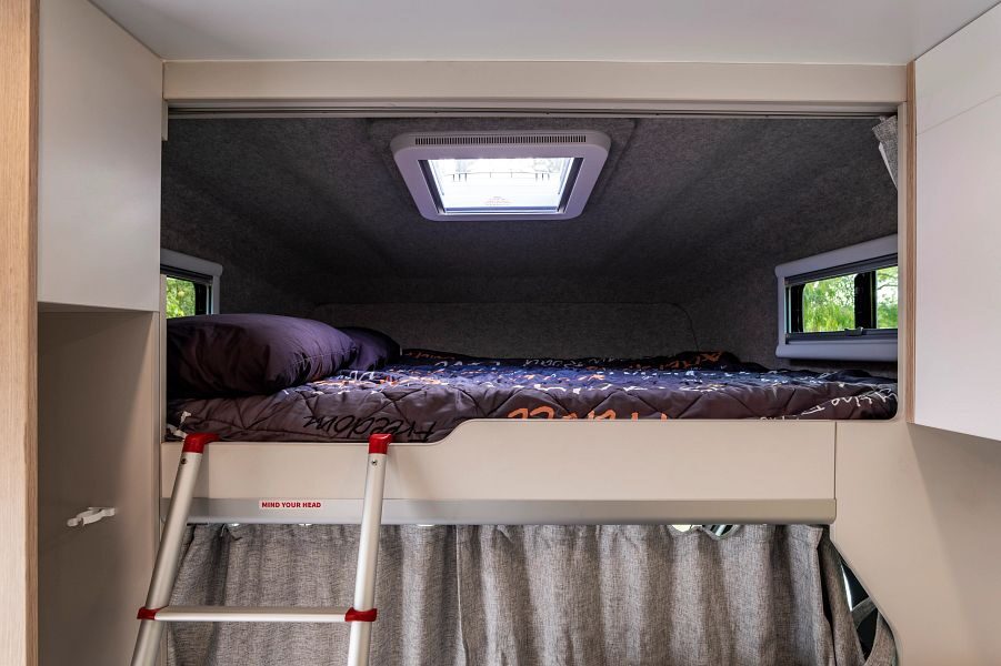 Een opgemaakt tweepersoonsbed in de alkoof met kleine ramen van de Maui Beach camper