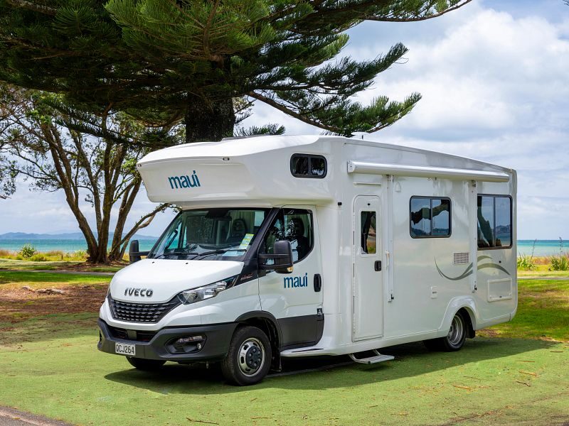 De zijkant en voorkant van de Maui Beach camper die geparkeerd staat naast een boom op een grasveld