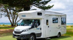 De zijkant en voorkant van de Maui Beach camper die geparkeerd staat naast een boom op een grasveld