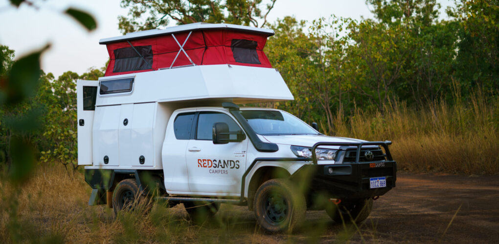 De camper op een gravelweg met zijaanzicht voor een tussenstop, het dak omhoog en de achterdeur geopend
