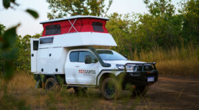De camper op een gravelweg met zijaanzicht voor een tussenstop, het dak omhoog en de achterdeur geopend