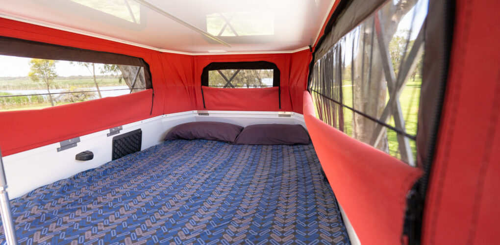 In de camper is een vast tweepersoonsbed met het dak omhoog gezet en aan de zijkanten en achterkant uitzicht naar buiten