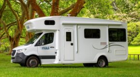 De zijkant van de Maui River camper voor zowel Australië als Nieuw-Zeeland geparkeerd op een grasveld onder een boom