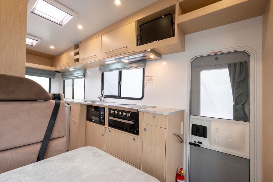 Het interieur van de Maui River camper gezien vanaf de zitplaats in het midden van de camper met zicht op de keuken en de deur naar buiten