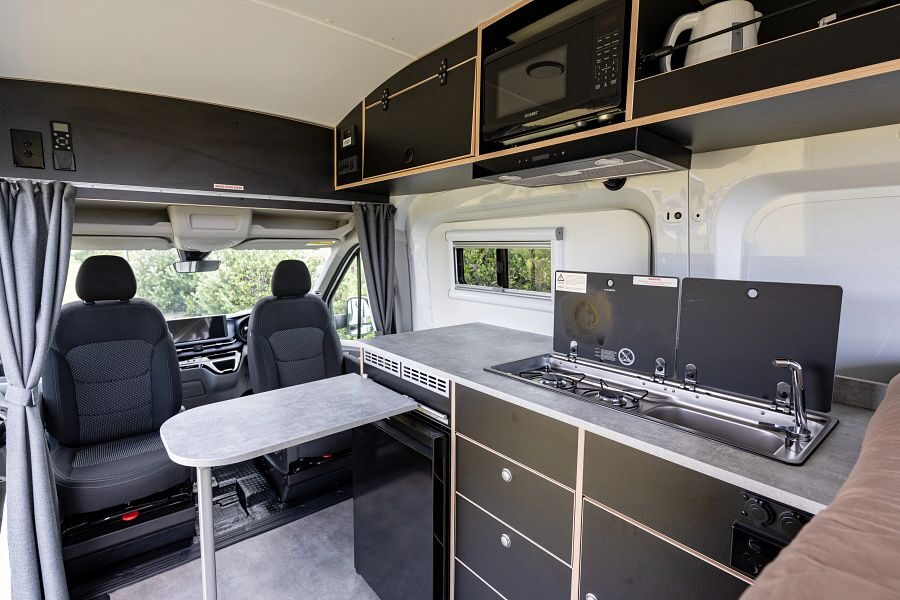 Het interieur van de Mighty Highball camper met tafel en keuken en draaibare bestuurderstoelen