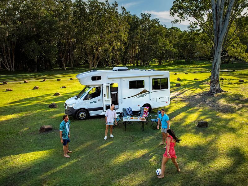 Een gezin is aan het voetballen voor de Maui Sunset Australië camper die geparkeerd staat op het gras