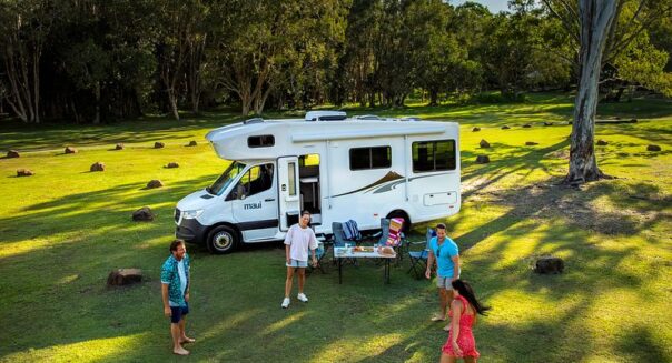 Een gezin is aan het voetballen voor de Maui Sunset Australië camper die geparkeerd staat op het gras