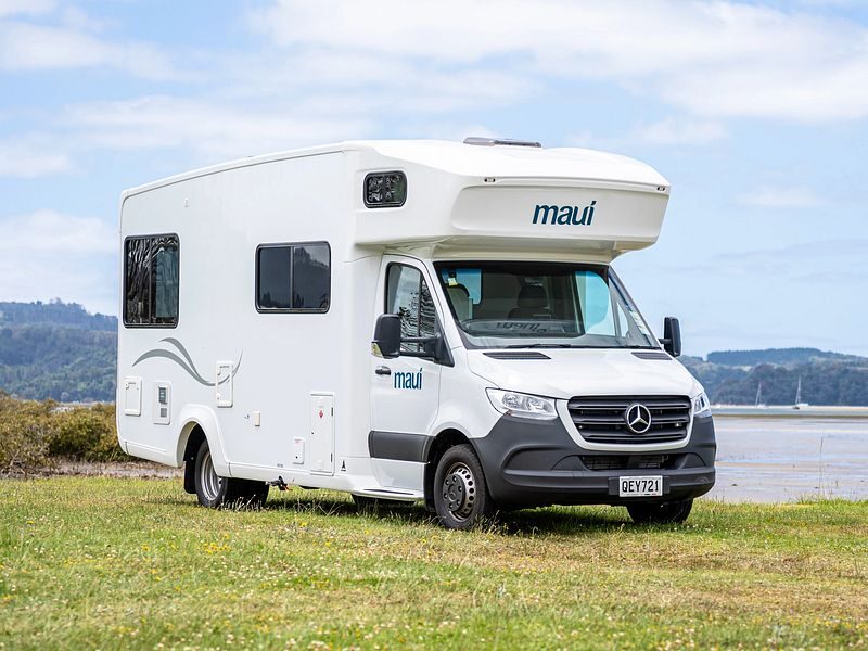 De Maui Sunset camper vanaf de voor- en zijkant geparkeerd langs het water op het gras in Australië