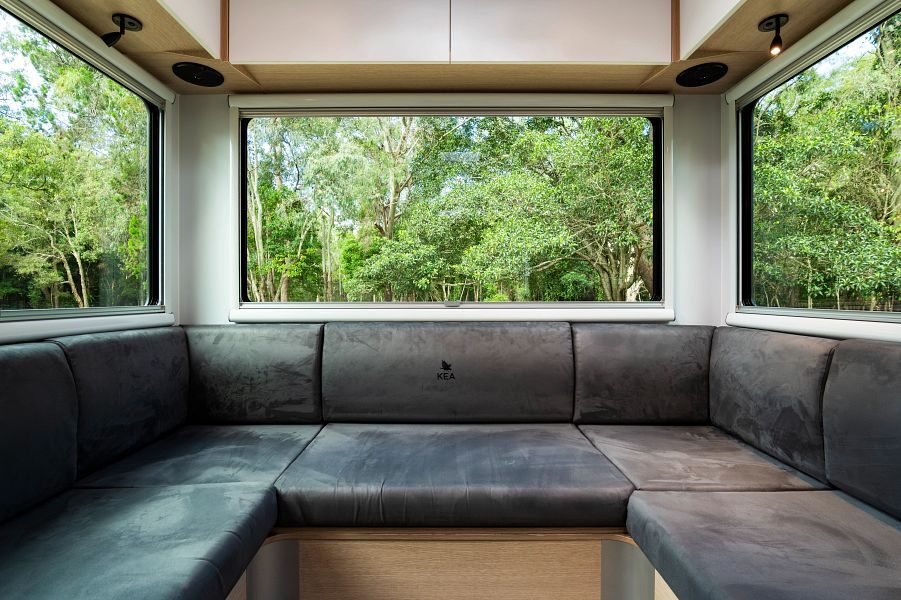 De zithoek in de achterkant van de Maui Sunset camper met grote ramen en uitzicht op bomen