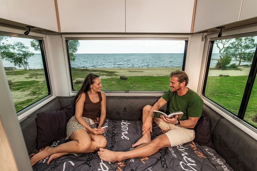 Een koppel zit op het tweepersoonsbed aan de achterkant van de Maui Sunset camper met uitzicht op de zee in Australië