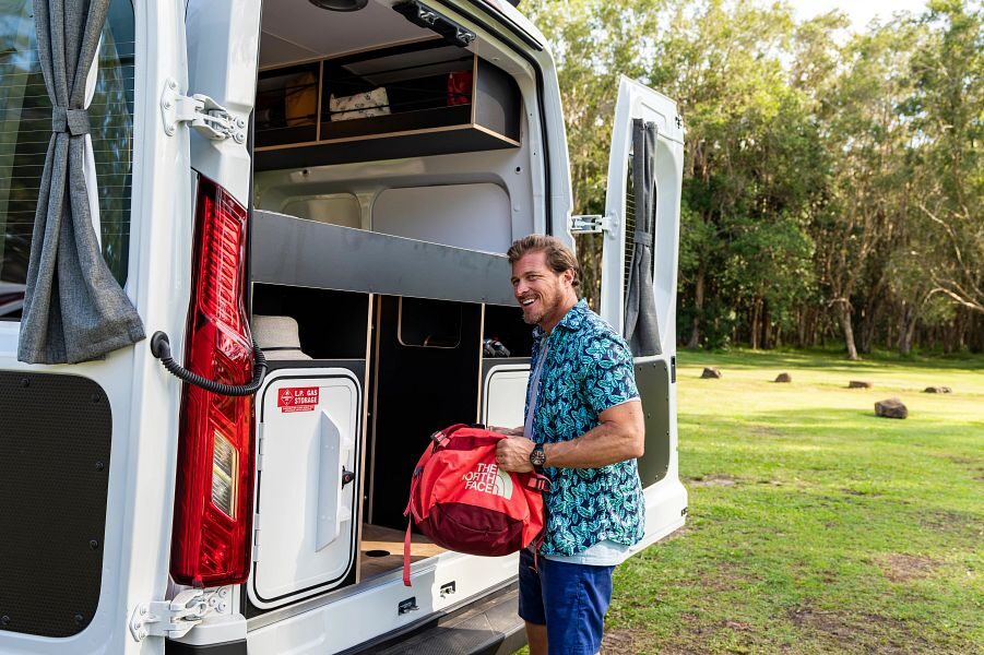 Een man bergt zijn tas op aan de achterkant van de Apollo Hitop camper in Australië