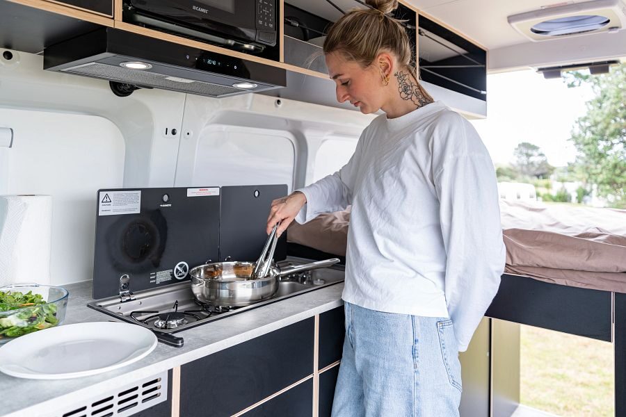 Een vrouw staat in de keuken en is aan het koken in de Apollo Hitop camper in Nieuw-Zeeland