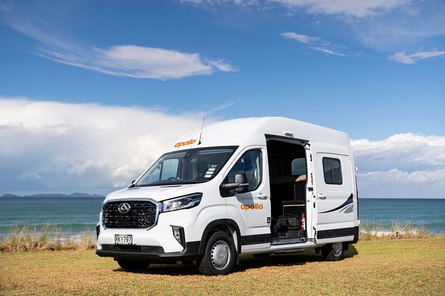De Apollo Hitop camper staat geparkeerd met de zijdeur open in het gras naast de zee in Nieuw-Zeeland