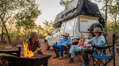 Een vriendengroep zit op de campingstoelen bij een kampvuur aan de achterkant van de Apollo 4WD Overland Camper in Australië
