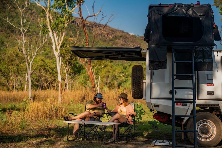 Een koppel zit op de campingstoelen aan de achterkant van de Apollo 4WD Overland Camper onder de luifel in Australië