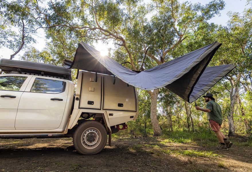 Een man klapt de luifel uit van de Apollo 4WD Overland Camper die geparkeerd staat in de natuur van Australië