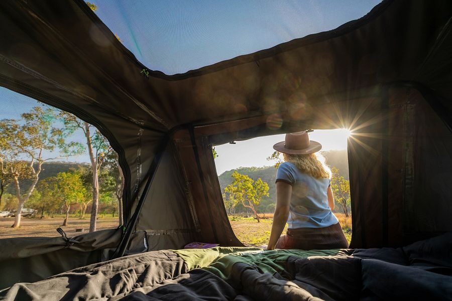 Een vrouw zit op de rand aan de binnenkant van de daktent op de Apollo 4WD Overland Camper in Australië