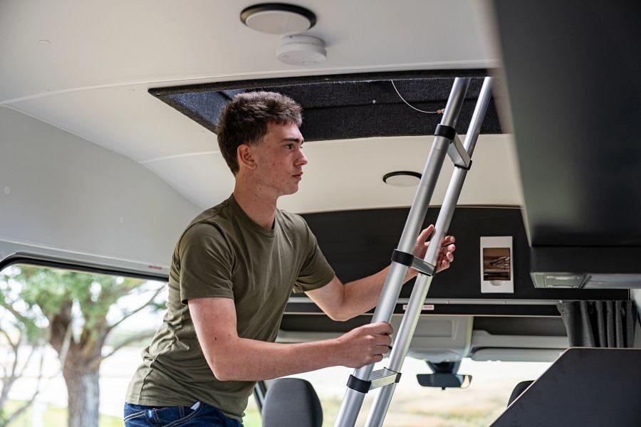 Een jongen klimt omhoog via een ladder binnenin de camper naar de daktent bovenop de Mighty Double Down