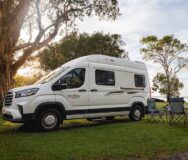 De Mighty Duo camper van de zijkant geparkeerd op het gras met twee campingstoelen en een tafel ernaast