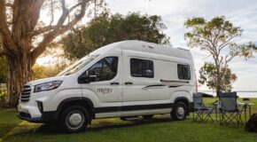 De Mighty Duo camper van de zijkant geparkeerd op het gras met twee campingstoelen en een tafel ernaast