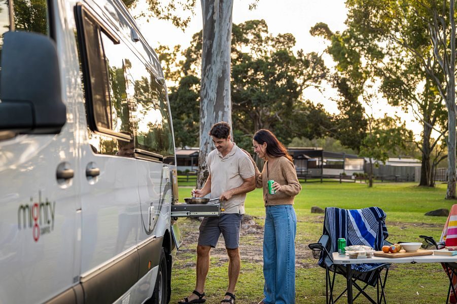 Een koppel is aan het koken in de buitenkeuken van de Mighty Deuce Plus camper in Australië