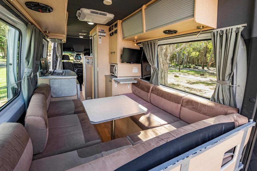 Vanuit de achterkant van de Mighty Deuce Plus camper kijk je vanuit de grote zithoek met tv en opbergruimte naar de voorkant van de camper