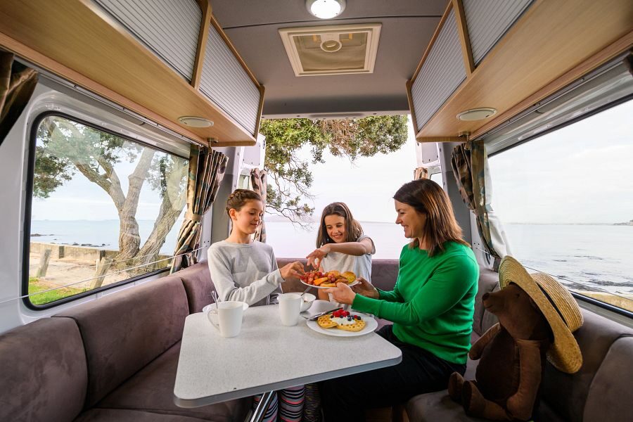 Een moeder is het aan het eten samen met haar kinderen in de zithoek aan de achterkant van de Mighty Deuce Plus camper