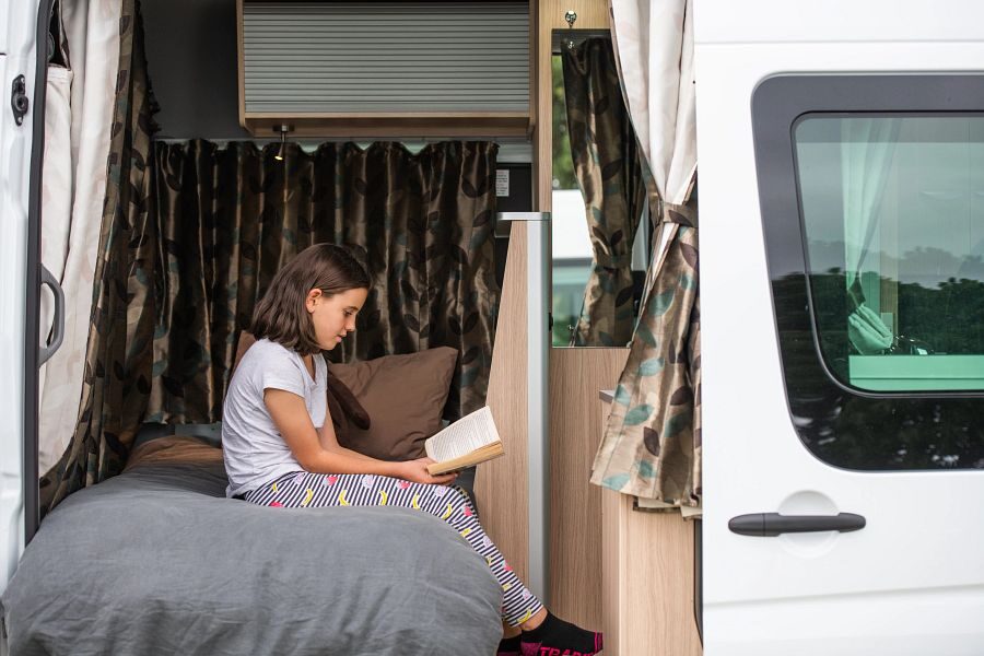 Een meisje is een boek aan het lezen op het eenpersoonsbed in de Mighty Deuce Plus camper