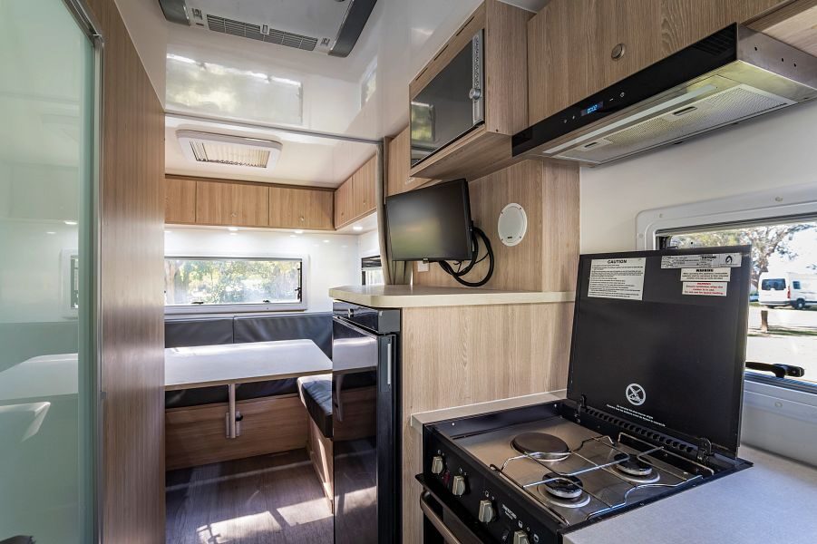 De keuken inclusief gaspitten en koelkast met daarboven een TV en magnetron in de Mighty Big Six camper