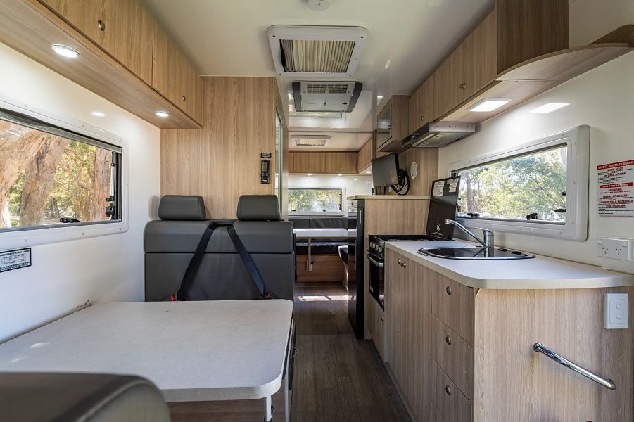 Vanuit de cabine kijk je naar de achterkant van de Mighty Big Six camper met zitplaatsen in het midden, de keuken en achterin een zithoek