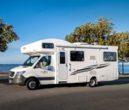 De zijkant van de Mighty Big Six camper die geparkeerd staat op een weg aan het water