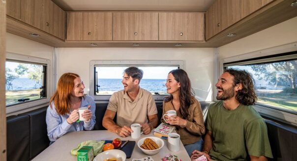 Twee stellen zitten in de zithoek van een camper met koffie en thee in de hand en een kaartspel