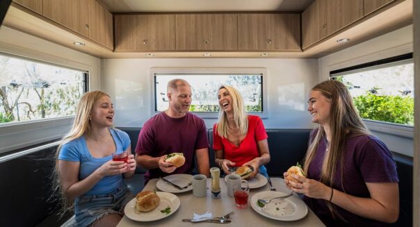 Man en vrouw met twee volwassen dochters zitten in de zithoek van de camper en eten lunch