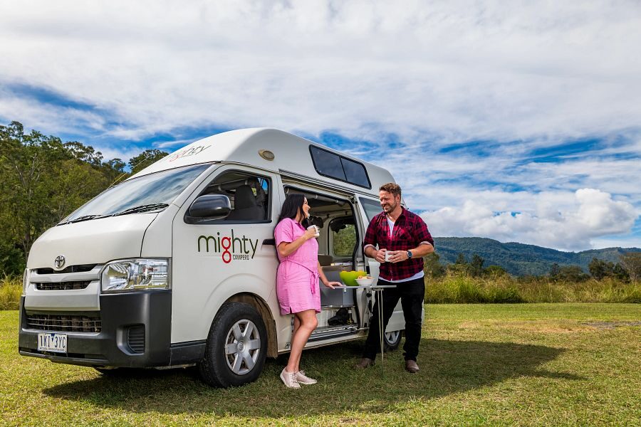 Een stel staat tegen de zijkant van de Mighty Lite HiLITE camper met een uitklapbare tafel in Australië