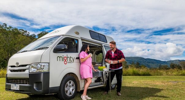 Een stel staat tegen de zijkant van de Mighty Lite HiLITE camper met een uitklapbare tafel in Australië