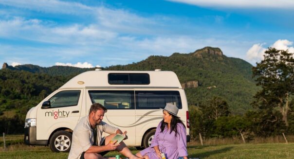 Een stel zit voor de Mighty Lite HiLITE camper op een picknickkleed in het gras in Australië
