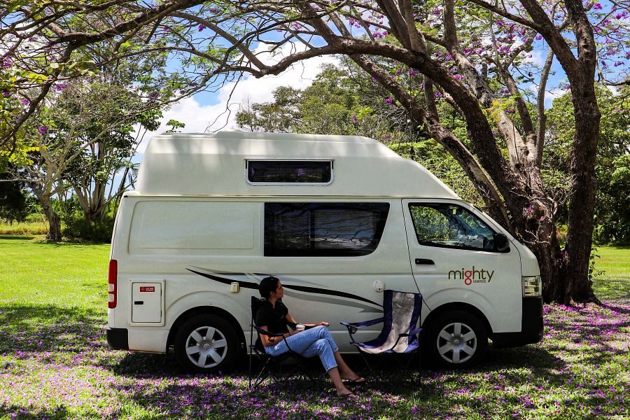 Een vrouw zit op een campingstoel aan de zijkant van de Mighty Lite DeLITE camper in Australië