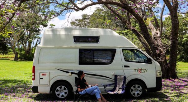 Een vrouw zit op een campingstoel aan de zijkant van de Mighty Lite DeLITE camper in Australië