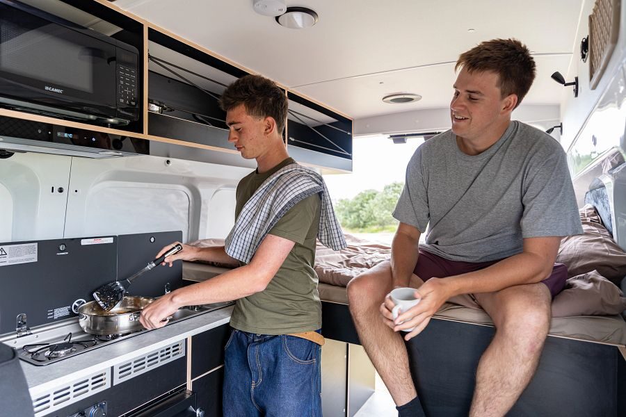 Een man is aan het koken terwijl zijn vriend op bed zit in de Mighty Lite DeLITE in Nieuw-Zeeland