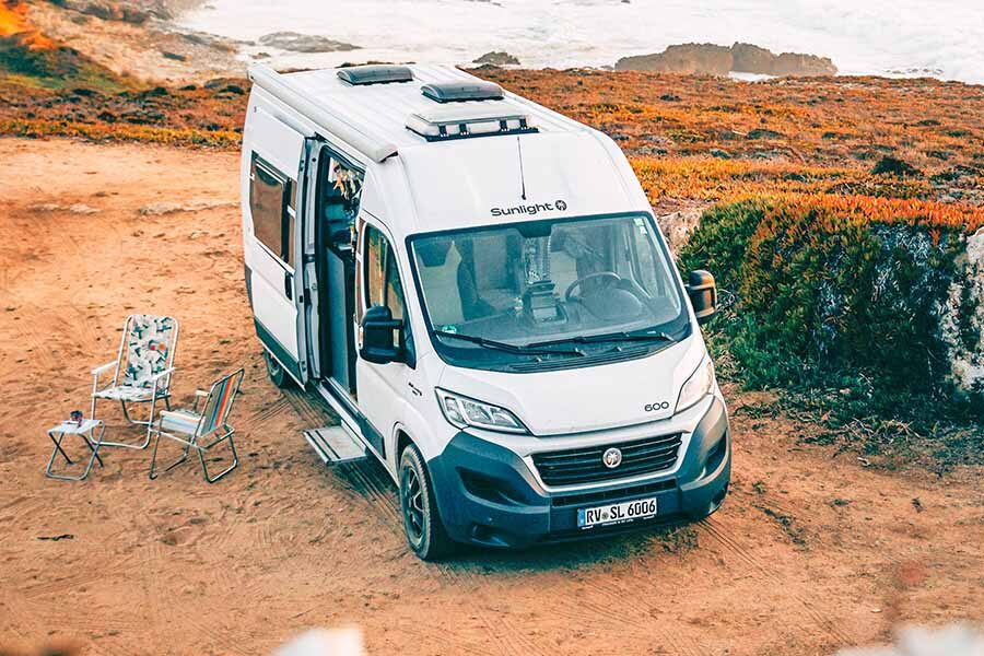 De McRent Urban Plus camper staat in het zand naast de zee met de zijdeur open en het voetstapje uitgeklapt