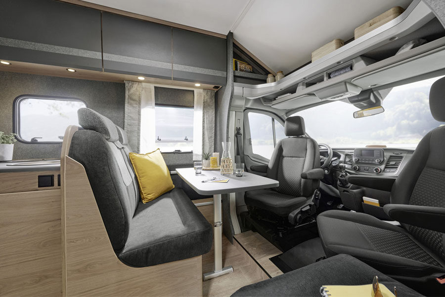 Het interieur aan de voorkant van de McRent Kiwi Compact camper met zitplaats en tafel en draaibare cabine stoelen