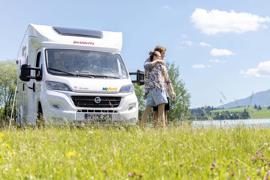 Een stel staat schuin voor de McRent Kiwi Compact camper te genieten van het uitzicht